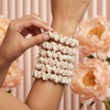 Person holding a set of cream hair scrunchies with flowers in the background