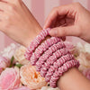 Pink hair scrunchies being worn on a wrist with a floral background