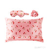 Glampton satin sleep set featuring a cherry-print satin pillowcase, matching satin eye mask, and satin scrunchie on a white background.